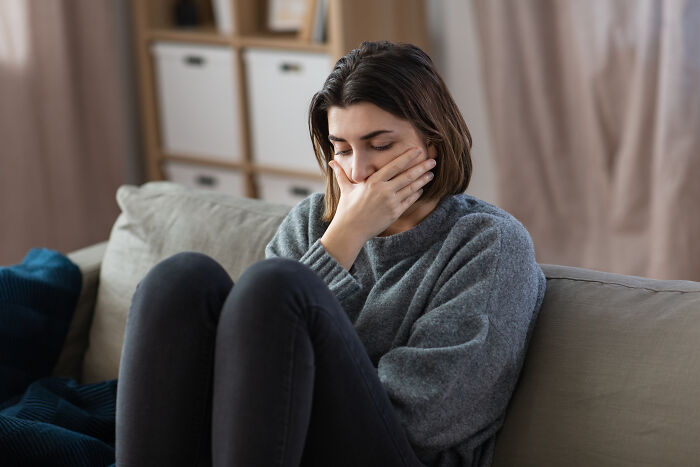Young woman sitting on couch, covering mouth with hand, appearing disturbed after people saw scary creepy situations.