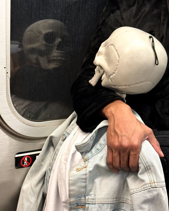 Person on New York subway holding a skull-shaped object with their reflection visible in the window.