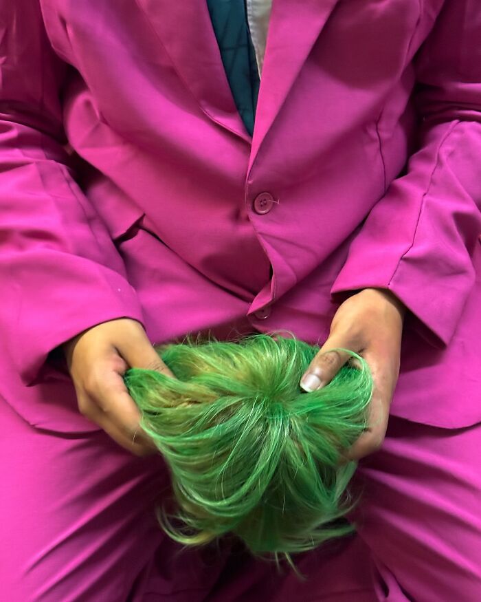 Person in a bright pink suit holding a vibrant green wig on the subway in New York, showcasing quirky items people carry.