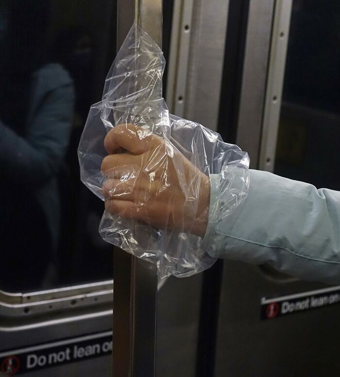 Person on New York subway holding a plastic bag over their hand while gripping a metal pole for support.