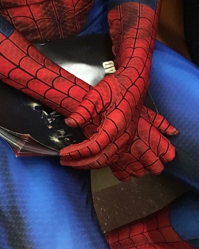 Person wearing a Spider-Man costume on the subway in New York holding a comic book in their hands.