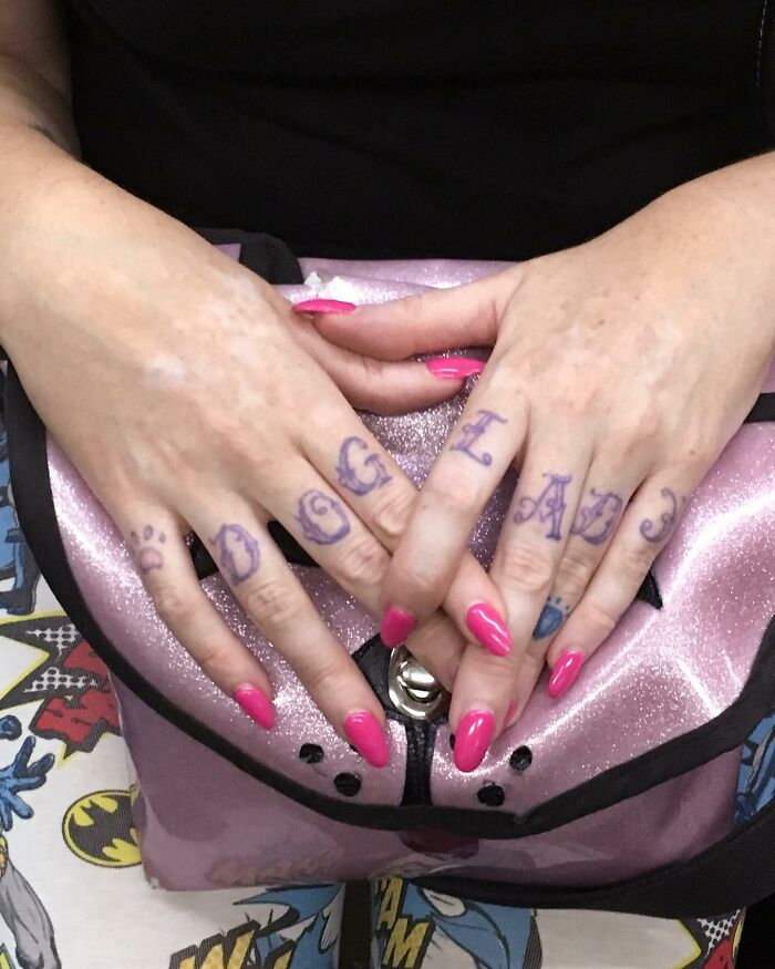 Hands with pink nails and tattooed letters on fingers resting on a shiny pink purse carried by a subway rider in New York.