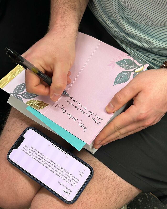 Person taking the subway in New York writing a card by hand while referencing a message on their phone.