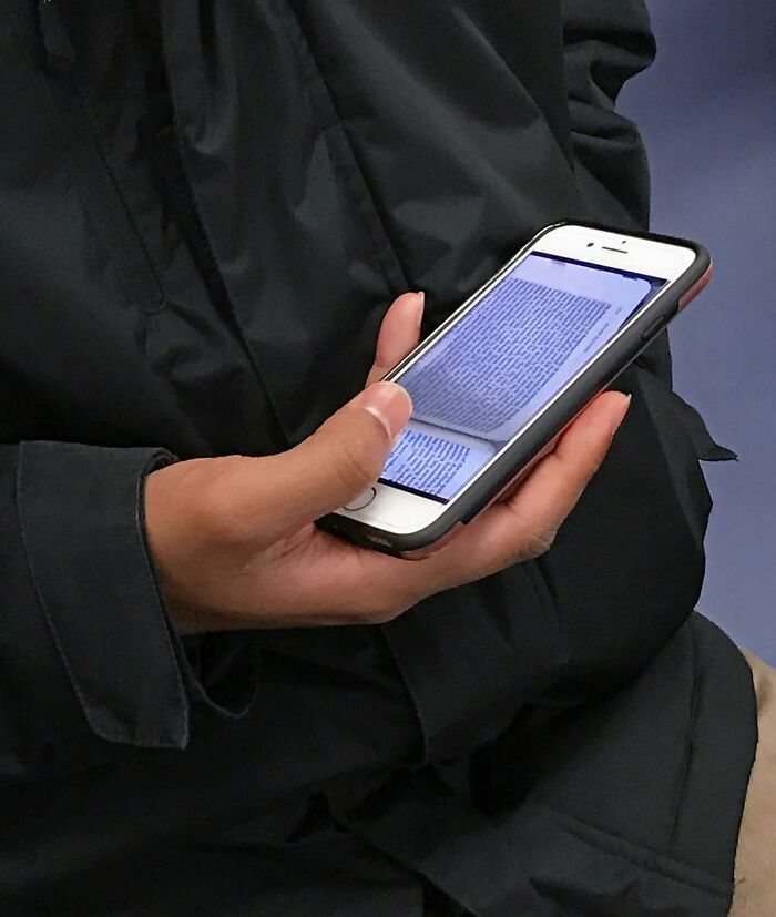 Person on New York subway holding smartphone showing a digital book, illustrating unique items people carry in their hands.