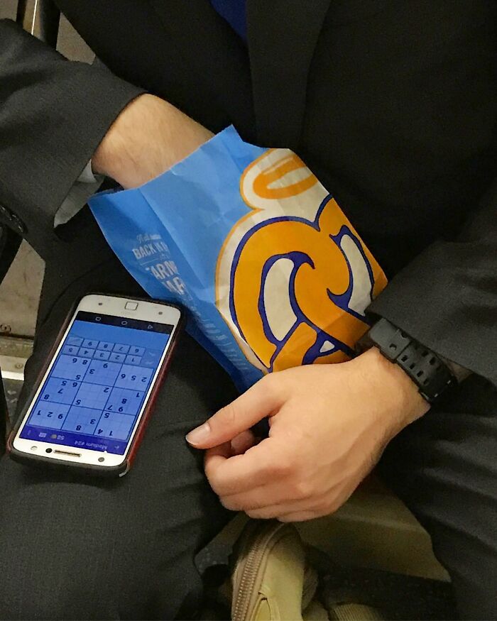 Person on New York subway holding a bag of pretzels and a phone with a Sudoku puzzle on screen.