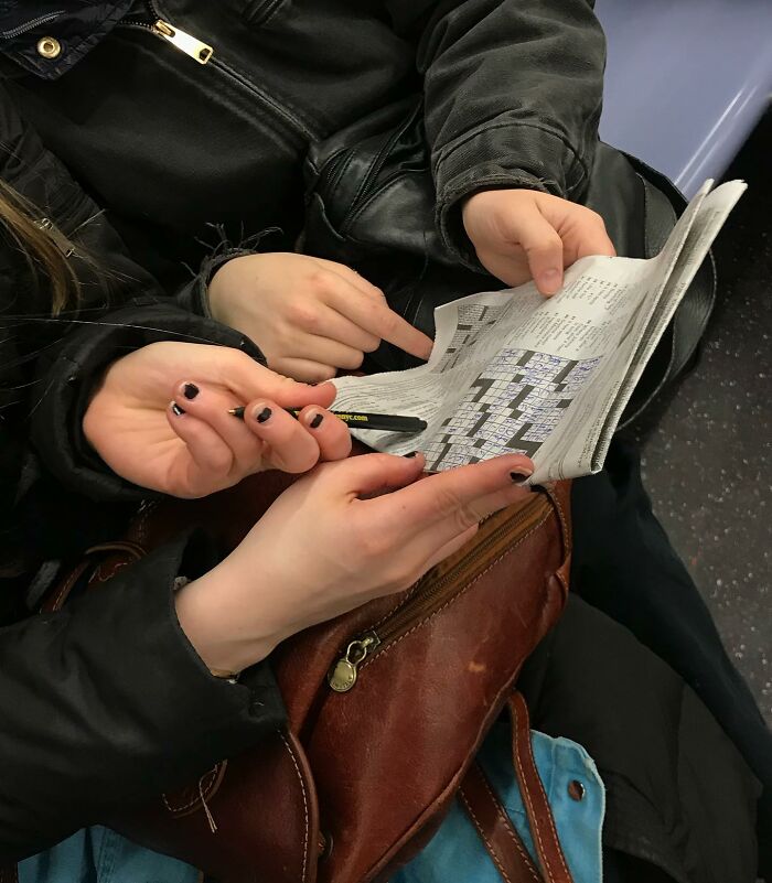 Two people on the subway in New York solving a crossword puzzle with a pen in their hands.