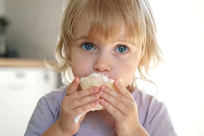 Young kid with nut allergy holding and eating ice cream sample indoors with a concerned expression on his face Young kid with nut allergy holding and eating ice cream sample indoors with a concerned expression on his face