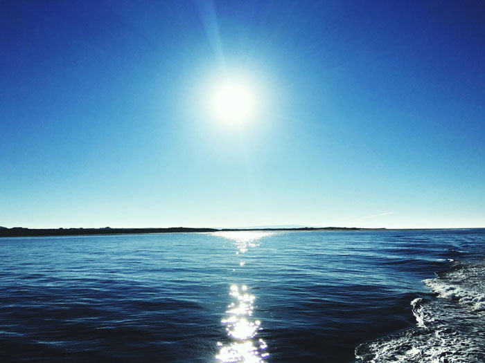 Bright sun shining over calm blue ocean with clear sky reflecting the time when the sun turned blue mystery.