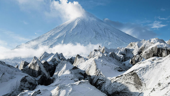 Snow-covered volcano under a blue sky with clouds, illustrating the mystery of the time when the sun turned blue.