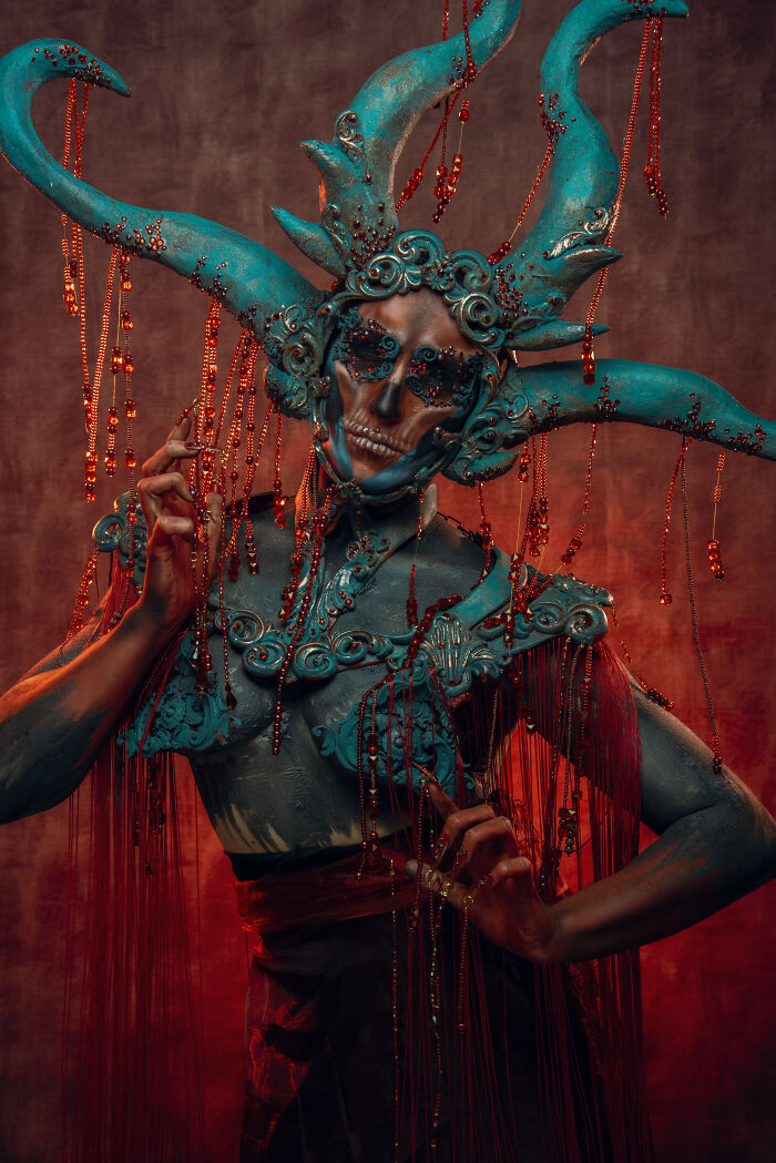 Person transformed into a haunting Halloween character with intricate turquoise horns and red bead decorations.