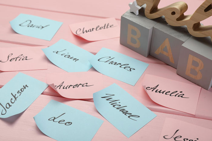 Colorful name cards scattered on a pink surface next to wooden blocks spelling BAB, highlighting baby-naming website trends.