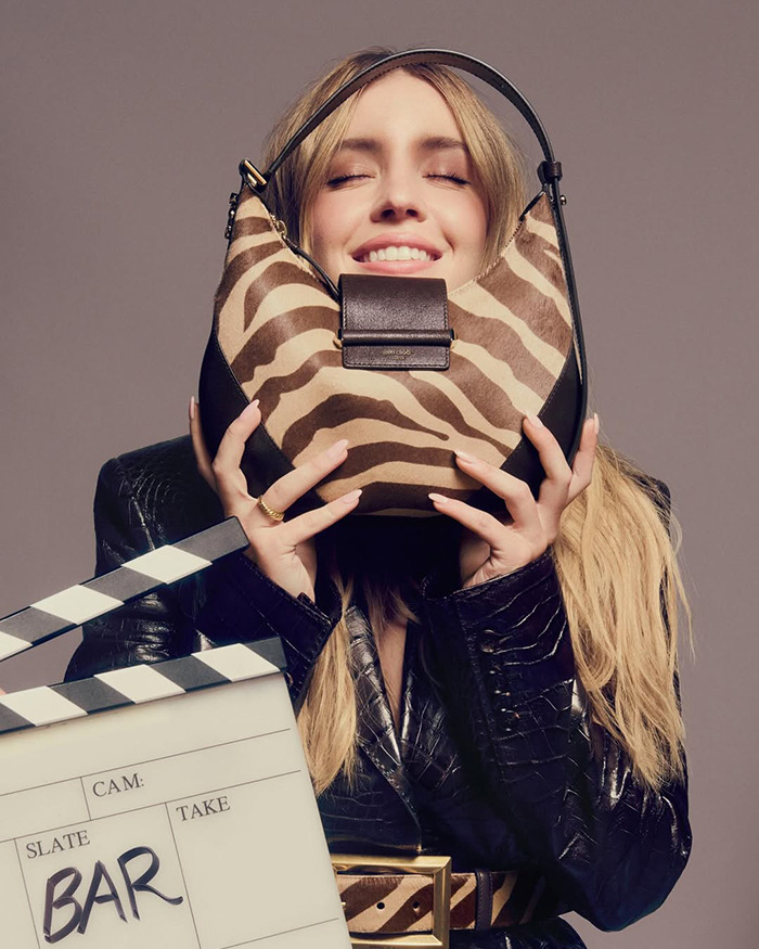 Sydney Sweeney holding a zebra-striped Jimmy Choo bag, smiling with eyes closed in a stylish black outfit. Sydney Sweeney holding a zebra-striped Jimmy Choo bag, smiling with eyes closed in a stylish black outfit.