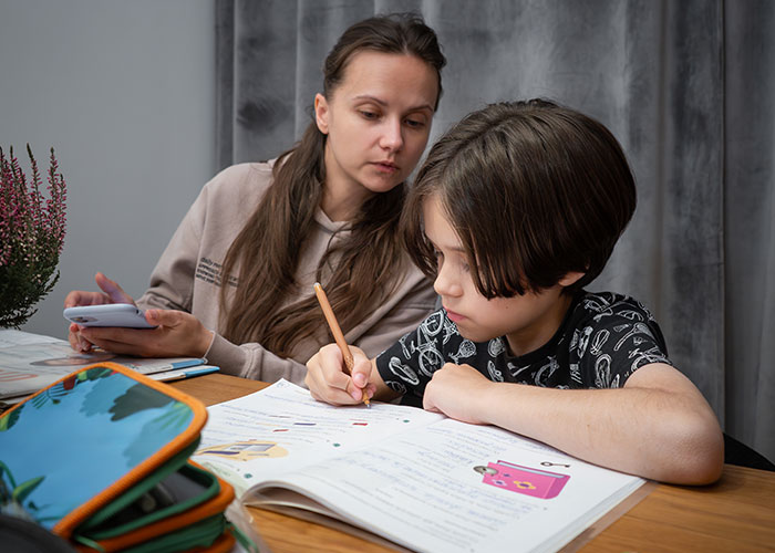 Young woman helping her sibling with homework, showing care and support while refusing assistance from their mother.