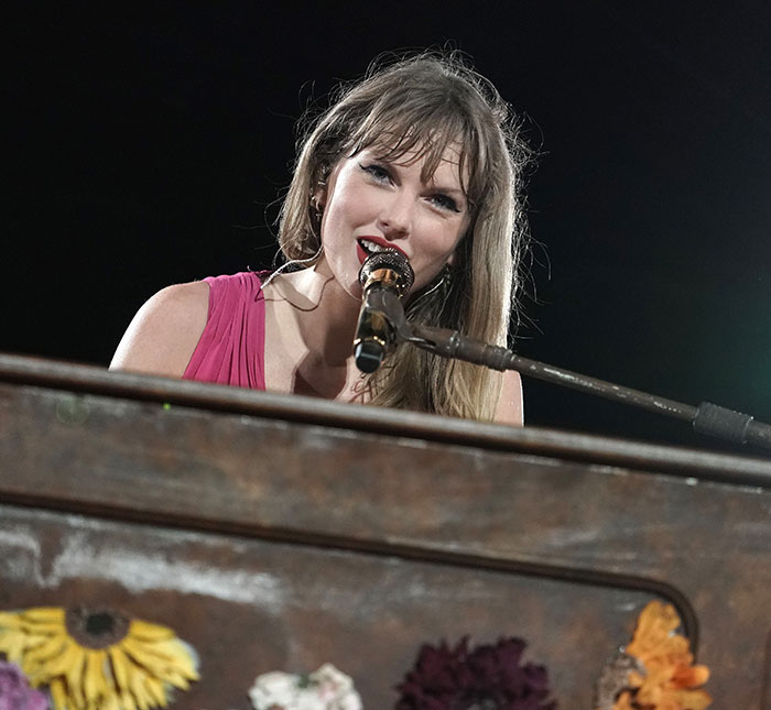Taylor Swift singing and playing piano during a live performance at night.