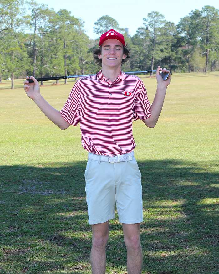Teen golfer in red striped shirt and cap posing on golf course holding club behind his shoulders on a sunny day