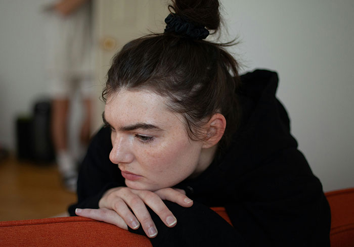 Woman looking worried and contemplative while leaning on a couch, reflecting on best friend&rsquo;s affair exposure to boyfriend