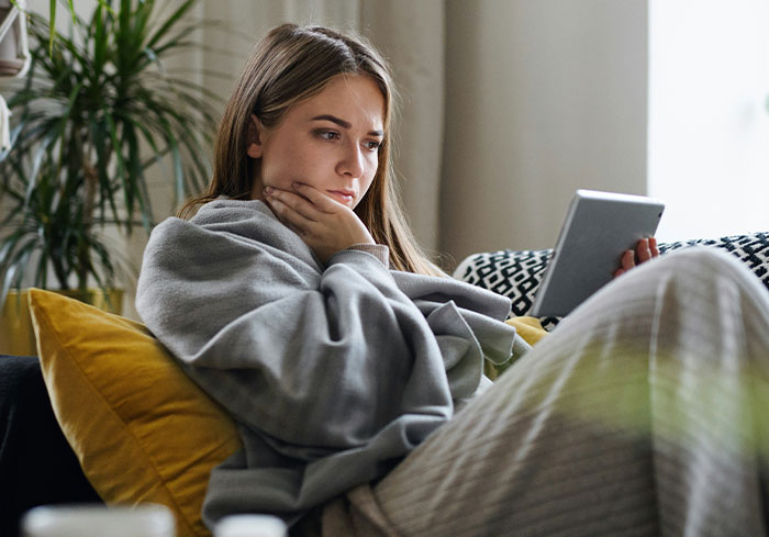 Woman looking concerned while reading on a tablet, reflecting on best friend&rsquo;s affair and relationship trust issues.