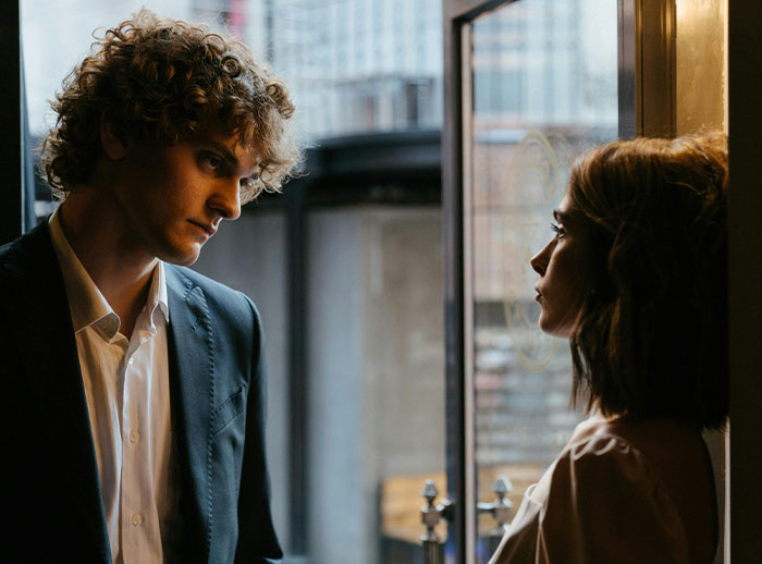 Man and woman facing each other near a window, illustrating tension related to exposing a best friend&rsquo;s affair to her boyfriend.