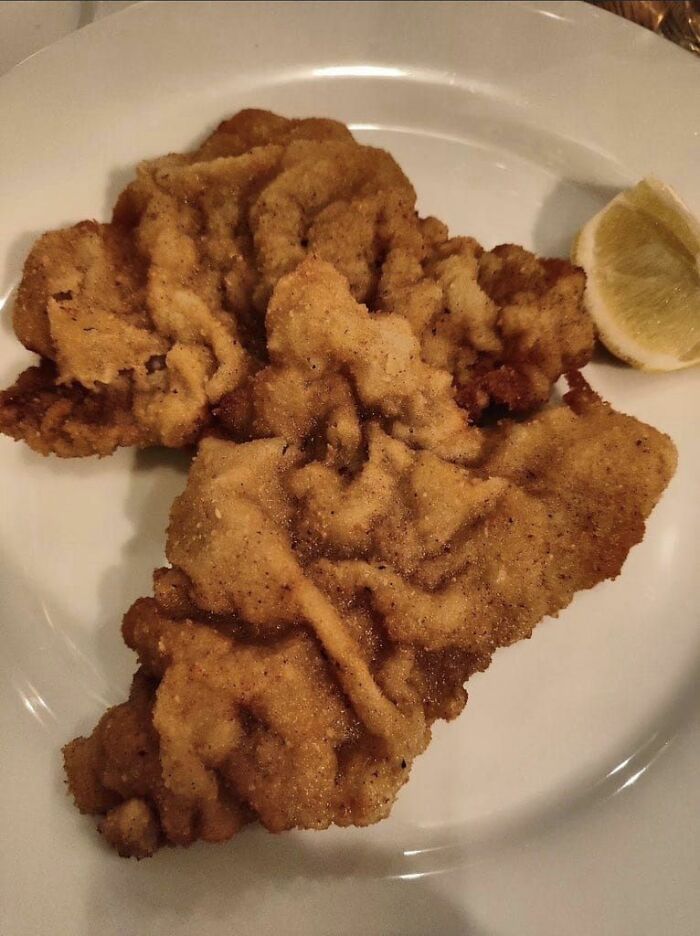 Breaded fried food resembling a distorted map shape served with a lemon wedge on a white plate, humorous map fail.