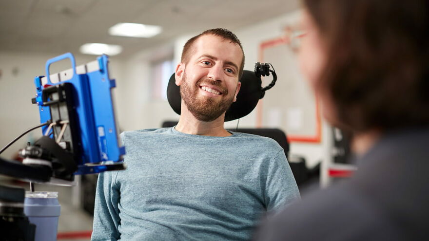 Man with ALS smiling while using a communication device, highlighting ALS and superfood wealth link research.