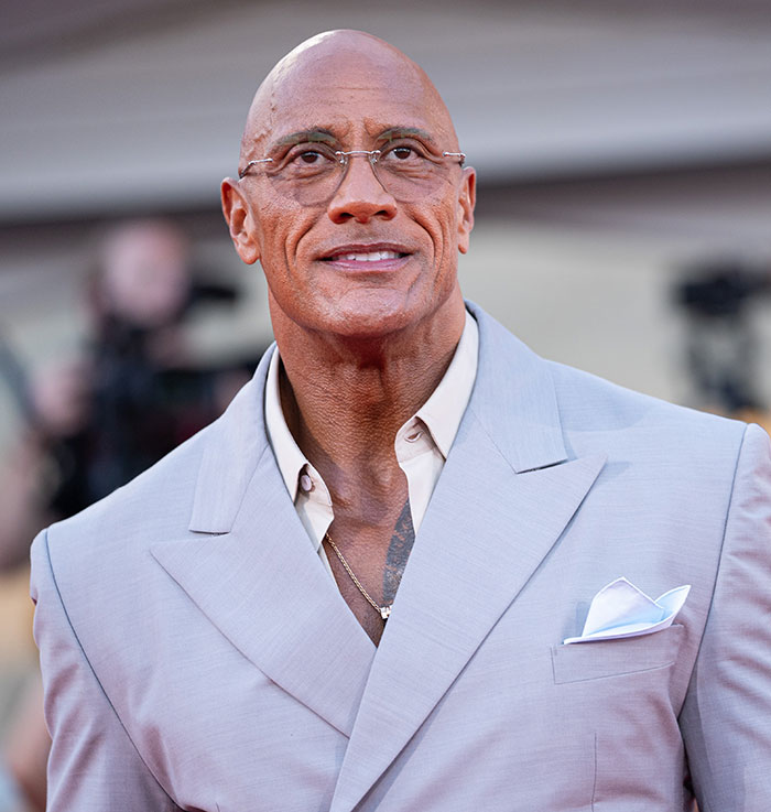 Dwayne Johnson wearing glasses and a light gray suit, attending an event amid fans defending his new slim look.