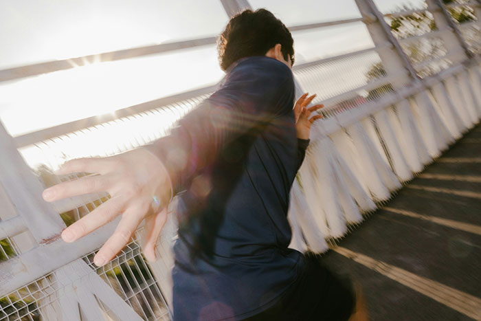 Person reaching out on a bridge with sunlight glare, illustrating things that look awesome in movies but terrible in real life.