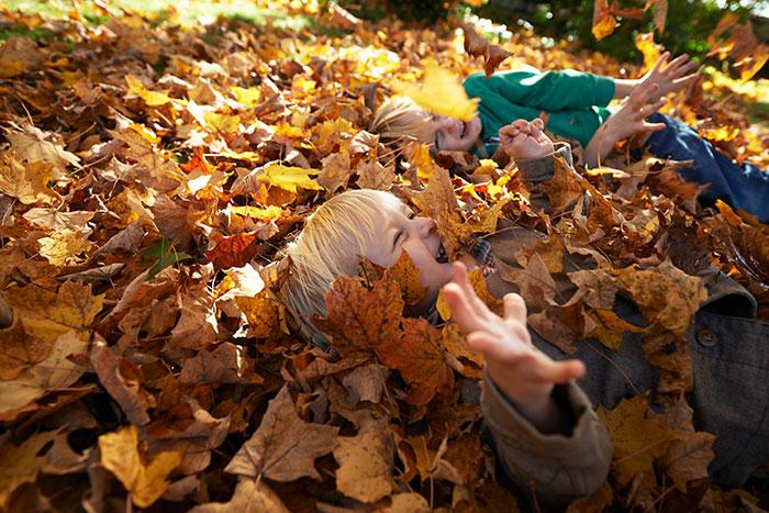 Two children playing and laughing in a pile of autumn leaves, showing things that look awesome in movies but not real life.