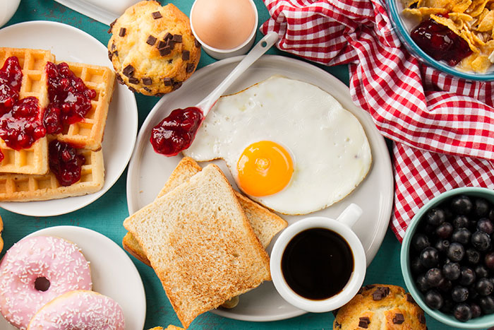 Breakfast spread with fried egg, toast, waffles, muffins, coffee, and berries illustrating things that look awesome in movies but not real life.