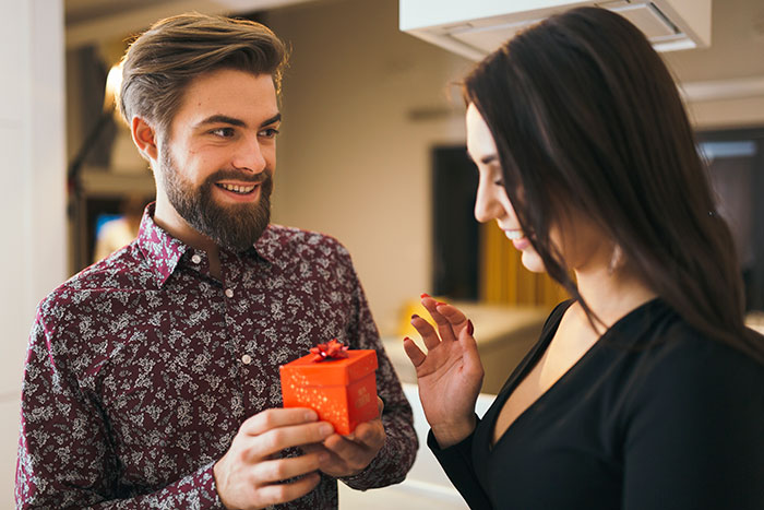 A man with a beard smiling while giving a small gift box to a woman, illustrating things that look awesome in movies.
