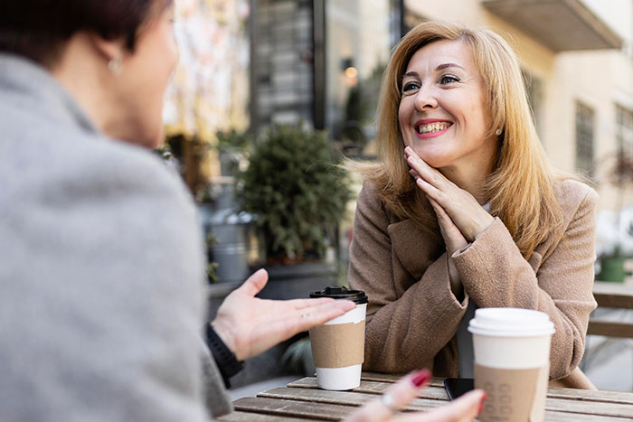 Two women enjoying coffee outside, smiling and chatting, showcasing things that look awesome in movies but are terrible in real life.
