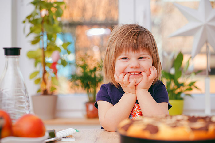 Smiling child sitting at a table with a pie and fruit, illustrating things that look awesome in movies but are terrible in real life.
