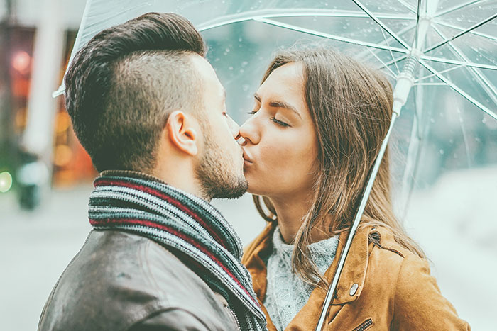 Couple sharing a romantic kiss under a transparent umbrella in the rain, highlighting things that look awesome in movies.