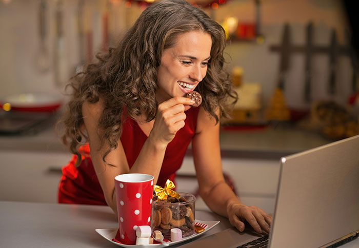 Woman enjoying cookies and hot drink while using laptop, illustrating things that look awesome in movies but are terrible in real life.