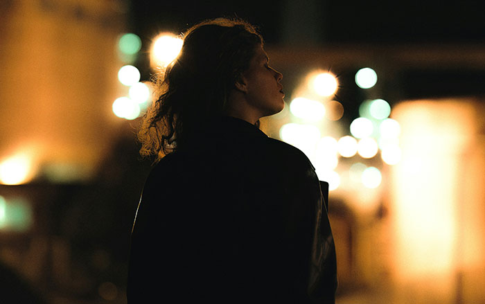 Woman standing alone at night in dim light, illustrating things men do that affect if women feel safe or threatened.