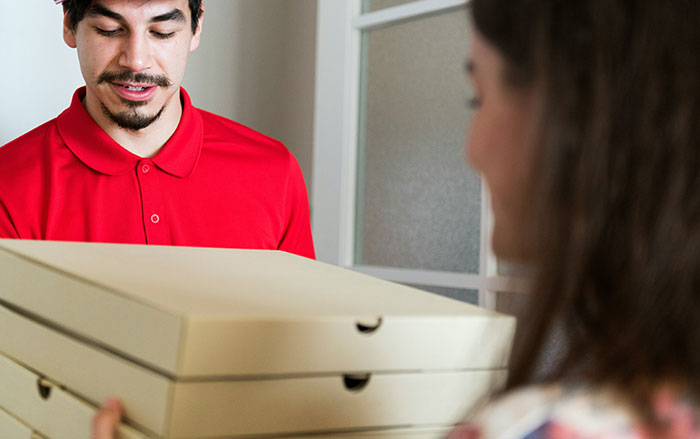 Man delivering pizza boxes to woman highlighting things men do that impact if women feel safe or threatened.