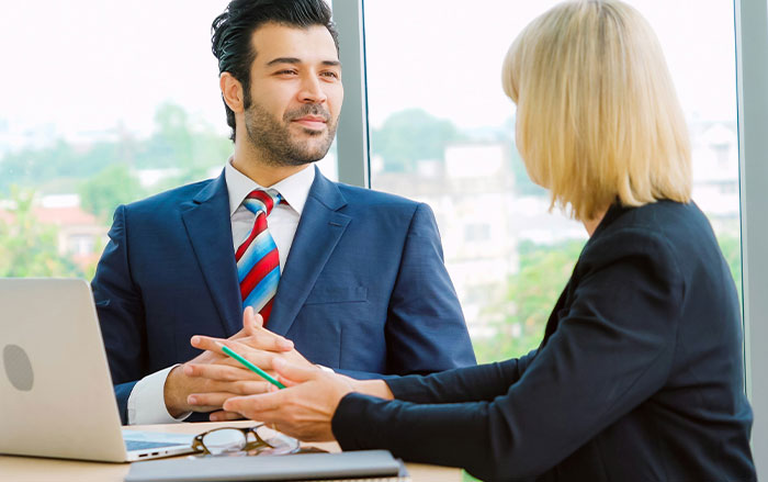 Man in a suit talking with woman in an office setting, illustrating things men do that affect women feeling safe or threatened.