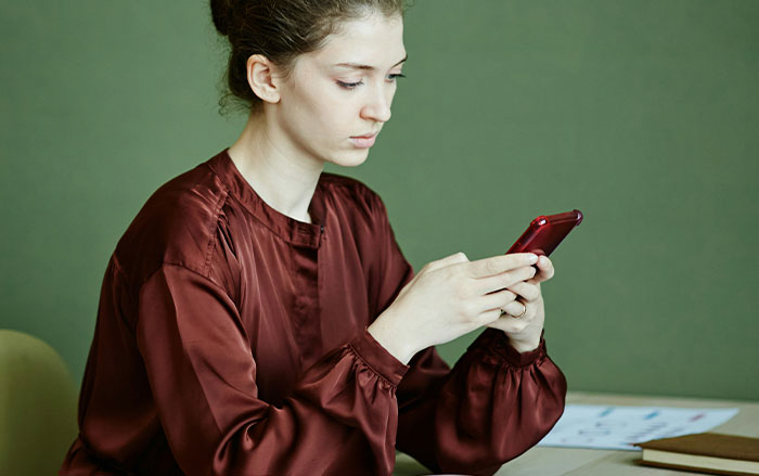 Young woman in a maroon blouse looking at a red phone, illustrating behaviors men do that affect women feeling safe or threatened.