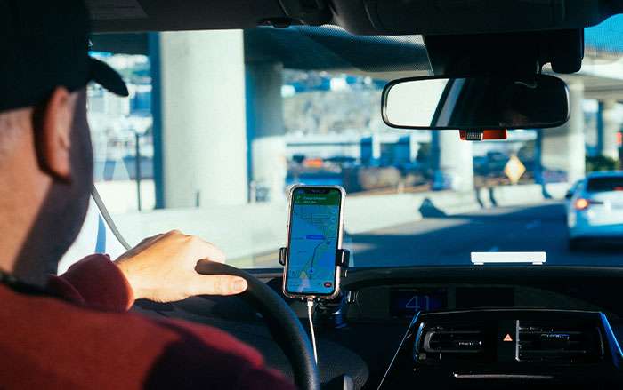 Man driving a car with a GPS navigation on phone, illustrating things men do without realizing impact on women's safety feelings.