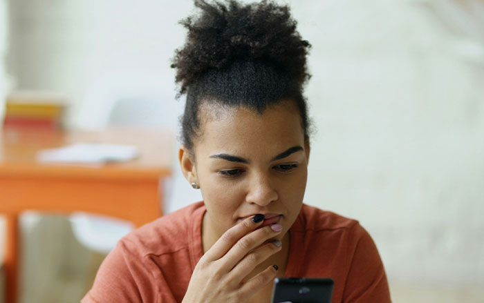 Young woman looking concerned while reading on her phone, reflecting on things men do affecting women's safety feelings.