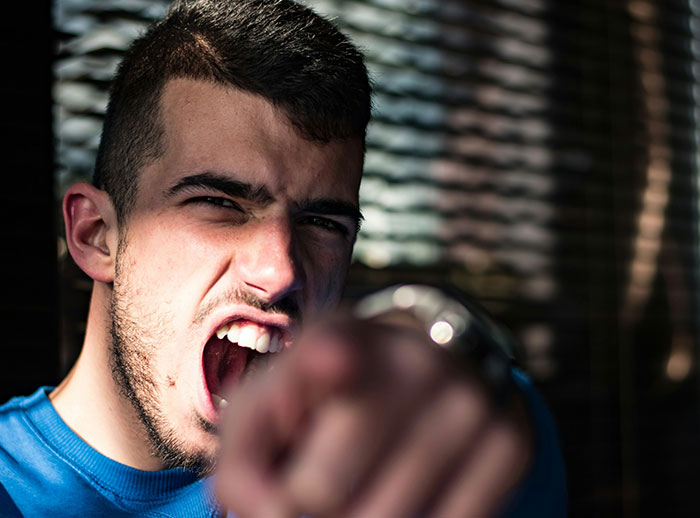 Young man in blue shirt yelling and pointing aggressively, illustrating behaviors that influence if women feel safe or threatened.