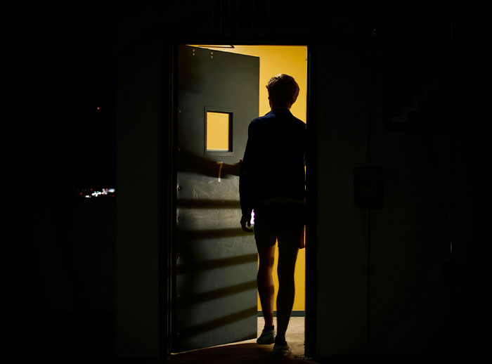 Man standing in a dark doorway with light behind, illustrating actions that affect if women feel safe or threatened.