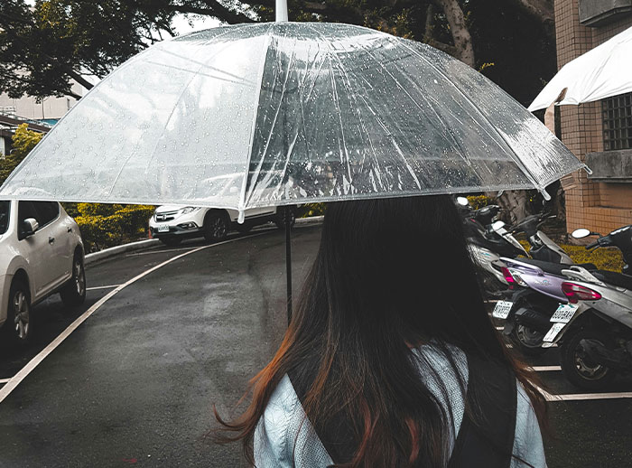 Woman holding a clear umbrella walking on a wet street, illustrating actions that affect if women feel safe or threatened by men.