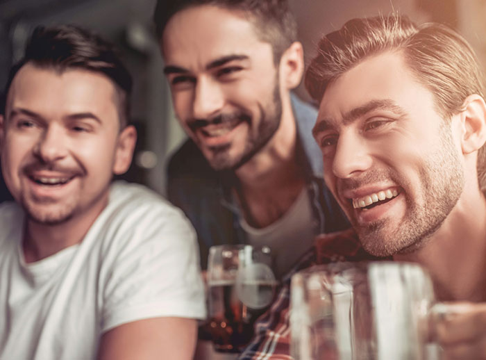 Three men smiling together in a social setting, illustrating behaviors that affect women feeling safe or threatened.