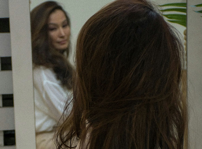 Woman looking at her reflection in a mirror, illustrating subtle behaviors that influence if women feel safe or threatened by men.