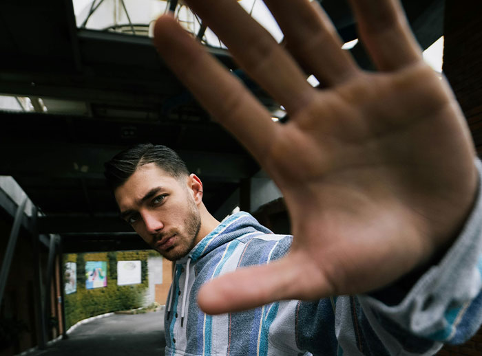 Young man raising hand in an urban setting, illustrating behaviors that decide if women feel safe or threatened.