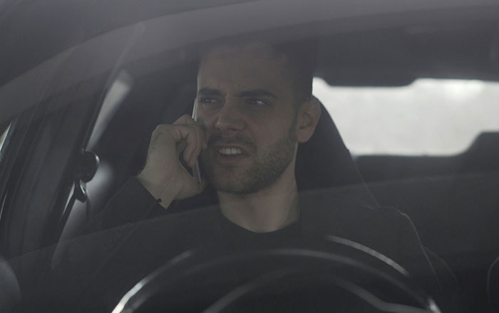 Man inside a car talking on phone with a tense expression, highlighting behaviors men do that affect women feeling safe or threatened.