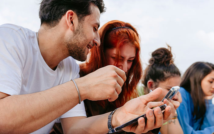 Group of young people outdoors, men and women using smartphones, illustrating things men do that impact women feeling safe or threatened.