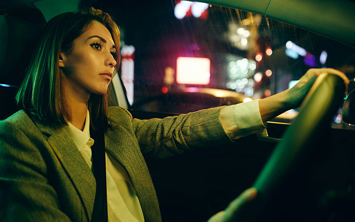 Woman driving at night looking cautious inside car, illustrating behaviors that affect women feeling safe or threatened.