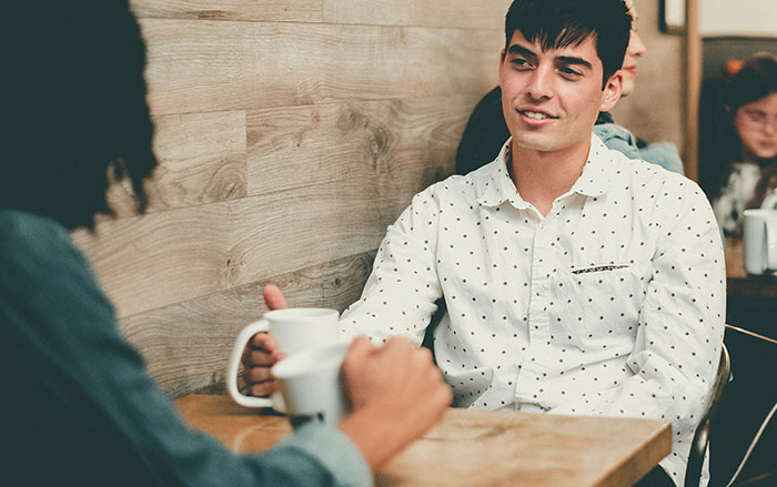 Two men having a casual conversation over coffee, illustrating things men do that affect whether women feel safe or threatened