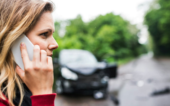 Woman on phone looking concerned near a damaged car on a road, illustrating things men do affecting women's sense of safety.